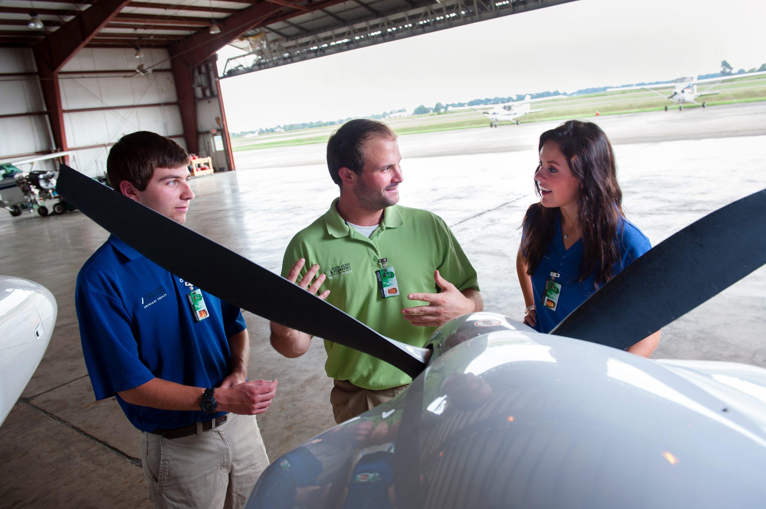 Instructor with two students standing in front of an plane in the airport hanger.