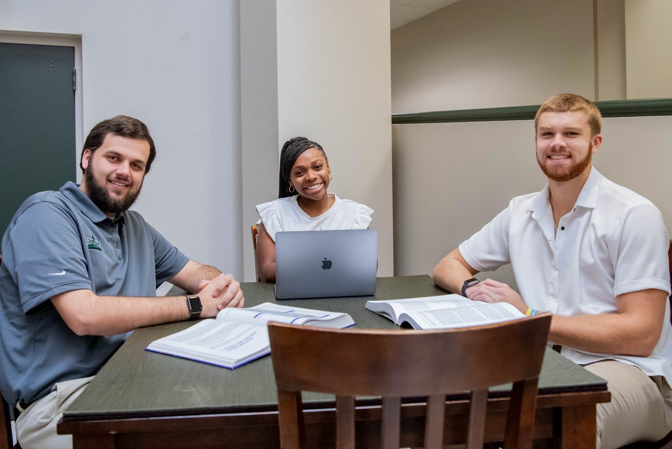 三名学生在商学院和航空学院的大厅里一起做作业, 带着笔记本电脑和两本课本.